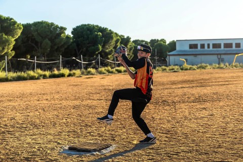 Boy pitching on a dusty baseball field in uniform and sport glasses, smiling as he throws a fast