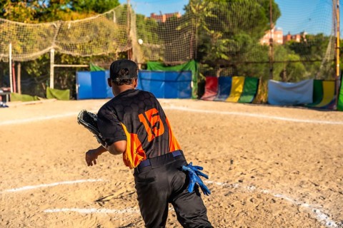 Player wearing a baseball uniform, cap, and fielding glove on a dirt field, throwing a ball during
