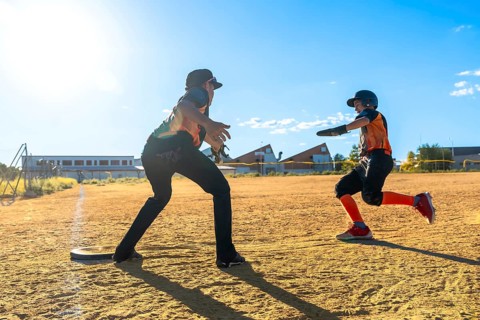 Youth baseball player sprinting hard across the dirt toward a base while coach or teammate awaits,