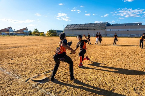 Young baseball players competing in a game on a sunny day, with one player sliding into second base