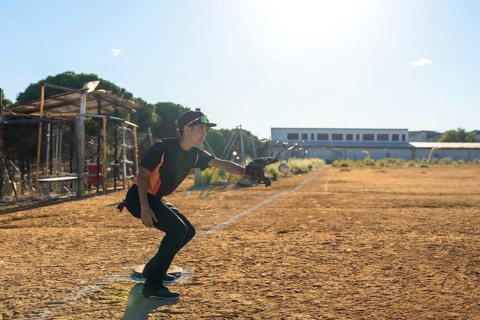 Baseball player in action on a dusty youth sports field, wearing uniform, cap and glove, extending