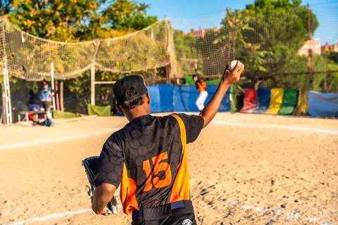 Young baseball pitcher in a black and orange uniform with number 15 on the back holding a ball