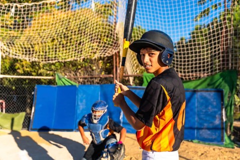 Young baseball batter wearing a helmet and looking at the camera while holding a bat, with a