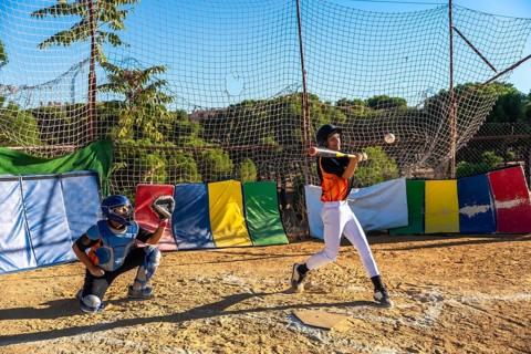 Young baseball players focusing on sport, with a batter hitting a baseball and a catcher ready