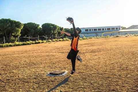 Young baseball player in uniform and glove jumping to catch a flying ball on a sunny dirt field,