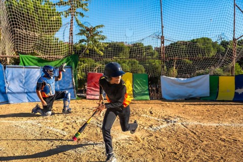 Kids playing baseball on a sunny day, an unidentifiable male batter wearing a helmet and looking