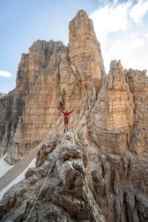 Mountaineer stretches his arms in the air, climbs an exposed rock in the secured Via Ferrata