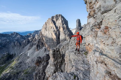 Mountaineer points into the distance, climbs an exposed rock band in the secured Via Ferrata