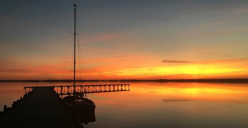 Tranquil Dümmer See with dock and sailboat at sunset, warm colors and calm atmosphere, Lembruch,