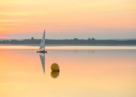 Sailing boat glides on quiet Dümmer Lake with a yellow buoy at sunset, Dümmer nature park Park,