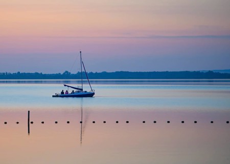 Sailing boat glides across quiet Dümmer Lake in the colors of a sunset, Dümmer nature park Park,