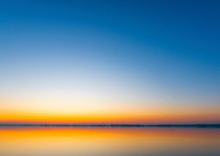 A calm sunrise with a soft color gradient is reflected in the still water of Lake Ddümmer, Dümmer