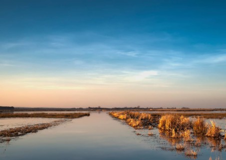 Extensive landscape with blue skies and delicate clouds is reflected in the water, soft yellow