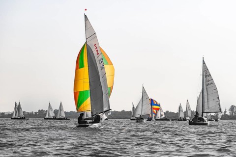Colourful sailboats in a wooden boat regatta on Lake Dümmer in grey skies, in the foreground a
