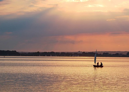 Two children 6 and 10 years old in a small red sailboat Optimist Jolle Opti on the Dümmer at golden