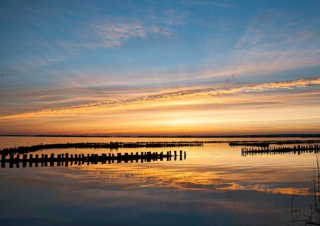 Sunset over water with impressive sky and light reflections, wooden posts reflected in the water,