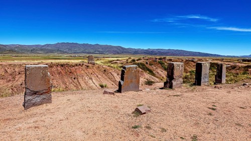 Standing stone monoliths overlook a vast open area with mountain backdrop, the archaeological site