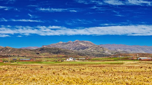 Wide fields in front of a mountain range under a cloudy sky, The Altiplano landscape in the Andes