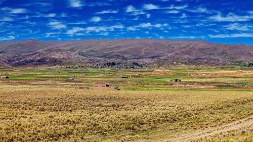 Wide fields against mountains and cloudy blue sky, The Altiplano landscape in the Andes of Bolivia