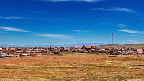 View of a village with church and antenna under wide sky surrounded by open fields, The city of