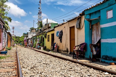 Tracks lead through residential area with bright houses and chairs outside under sunny skies,