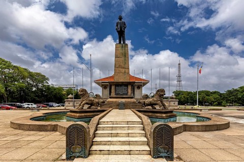 A monument with a statue on a pedestal surrounded by lions and a fountain on a cloudy day, Colombo