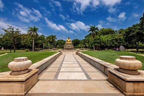 Quiet park with centrally placed Buddha statue and stone path under blue sky, The Golden Buddha in