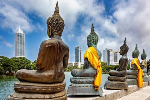 Buddha statues in bronze with yellow cloths in front of skyscrapers and water, The Seema Malaka