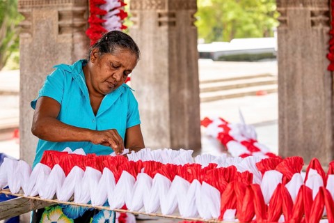 Woman making red and white decorations in an enclosed space, people making garlands in Colombo Sri
