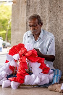 Elderly man sitting and concentrating making flowers, people making garlands in Colombo Sri Lanka