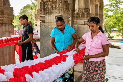 Women making traditional decorations in a temple-like building, people making garlands in Colombo