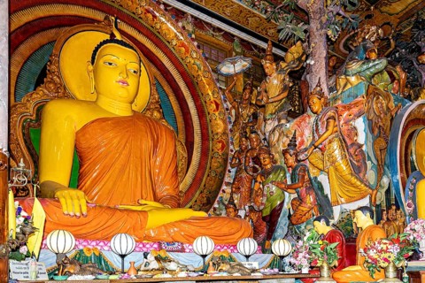 Buddha statue on an altar surrounded by frescoes and religious figures in a spiritual and colorful