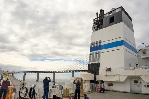 Passengers on a ship with a view of the Øresund Bridge, a ferry under a massive bridge structure of