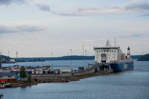 Large ferry in Naantali harbor on the water, surrounded by various buildings and a cloudy sky,