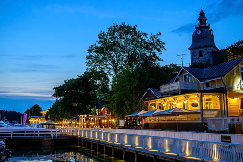 Street scene on Naantali harbour promenade, illuminated buildings and waterside boats at dusk, with