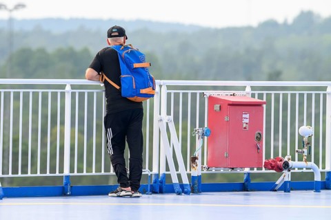 Man with blue backpack on deck of Finnlines ferry Naantali Kappelskär, overlooking wooded