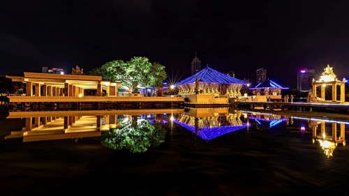 Nocturnal scene with illuminated pavilions, reflections in the water and city in the background,