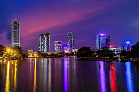 Nighttime city view with brightly lit skyscrapers and colorful sky mirror in the water, the skyline