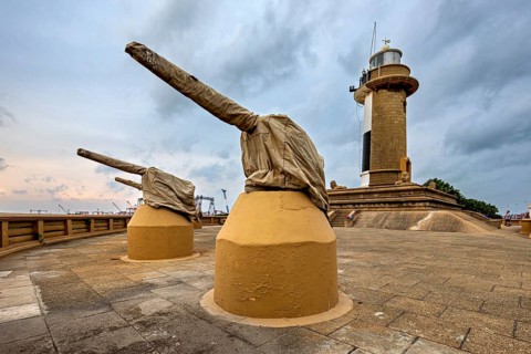 A lighthouse next to two cannons on a paved area under a cloudy sky, The Colombo Sri Lanka