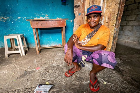 Smiling man wearing cap squats relaxed in a simple room, people in the streets of Slave Island in