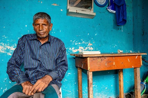Man sitting relaxed in front of a blue wall in a simple room, people in the streets of Slave Island