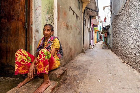 Elderly woman sitting pensively in a narrow alley, people in the streets of Slave Island in Colombo
