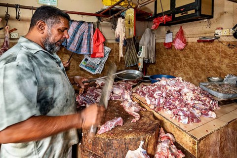 A butcher shreds pieces of meat with a cleaver on a wooden table in a traditional market