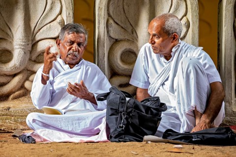 Two men in white robes are engaged in discussing in front of an artfully decorated temple, praying