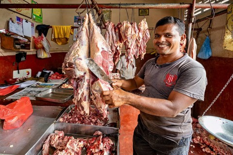 A smiling butcher cuts meat in a traditional shop, with pieces of meat around him, butcher shop in