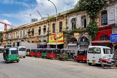 Busy urban street with old buildings and a series of tuk-tuks including a cloudy sky, tuk tuk in