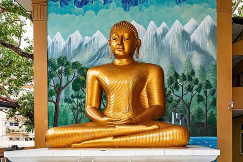 Golden Buddha statue in front of a painted wall with landscape motif, The Seema Malaka temple with