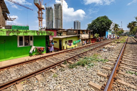 Railway tracks next to colorful houses with skyscrapers in the background and construction crane