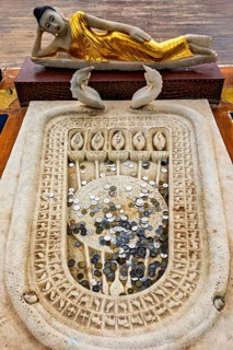 A reclining Buddha statue with gold robes above a carved stone surface filled with coins,