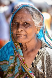 Elderly woman wearing a blue sari with a serious expression and traditional jewelry, portrait of an